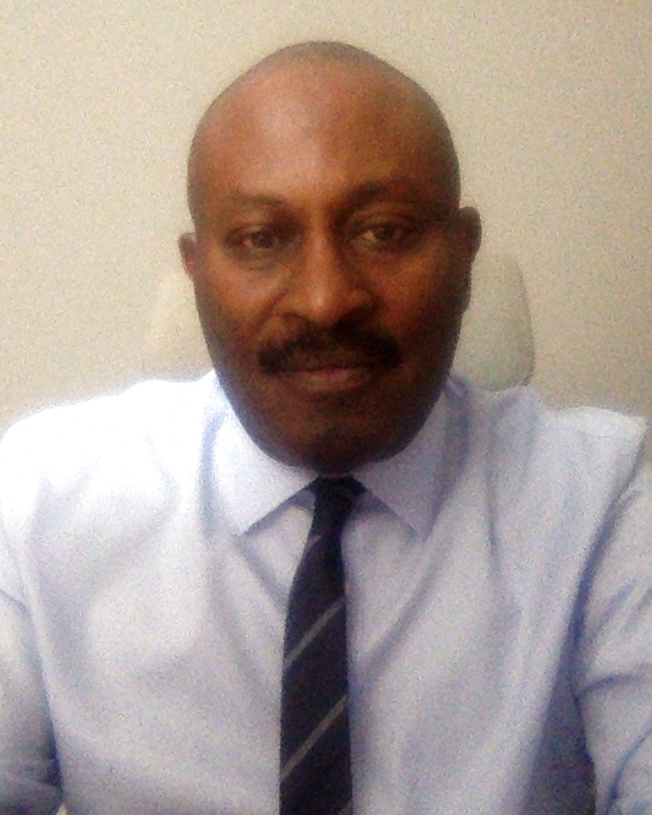 Henry Adu Bobi, Cognitive Behavioural Psychotherapist, in his consulting room. Wearing a blue shirt.